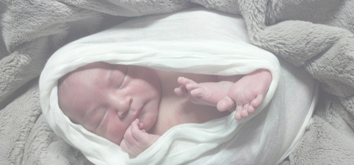 Newborn baby swaddled in a white blanket, laying on top of a fuzzy grey blanket